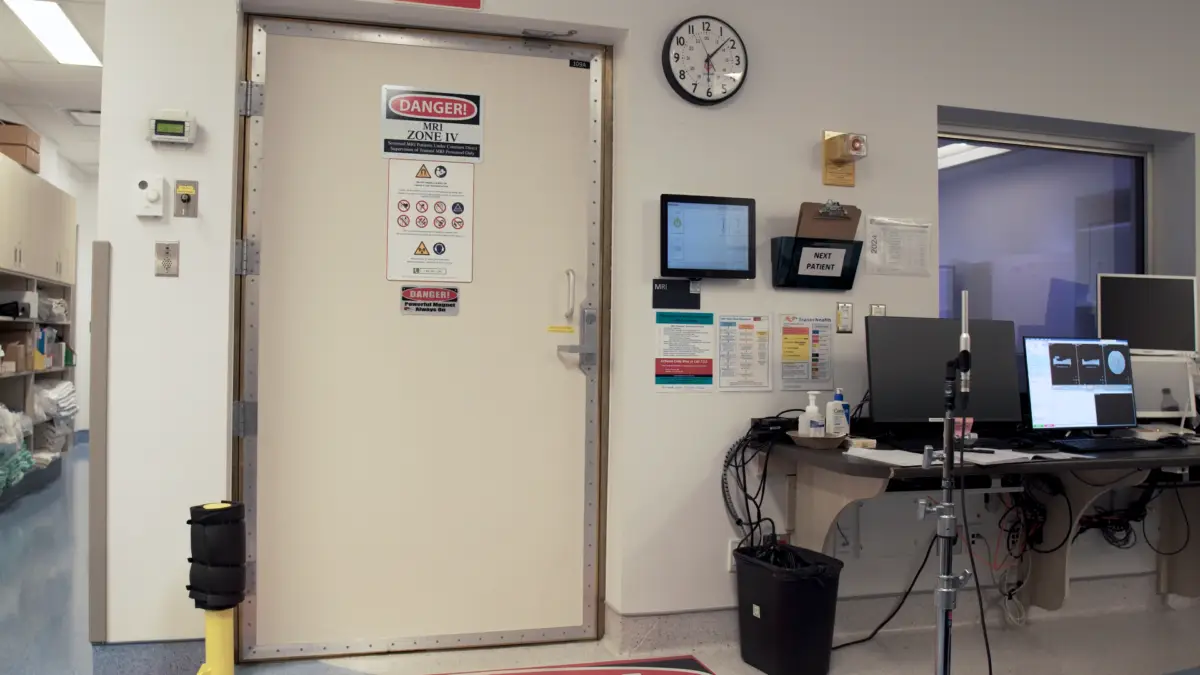 The thin copper door lacks acoustic insulation, allowing noise to escape into the control room. Installing an acoustic barn door inside the MRI room can significantly improve sound isolation by providing an additional barrier that reduces airborne noise leakage. This solution enhances acoustic performance while maintaining accessibility to the scanner room.